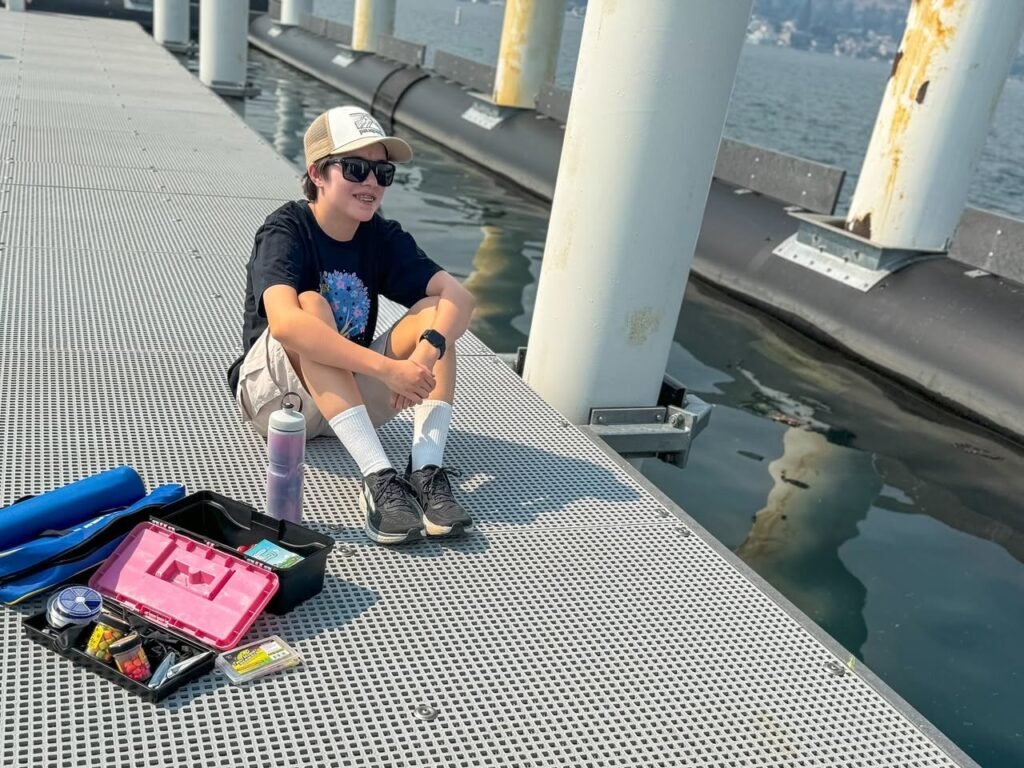 A person resting on a metal grate walkway near water with travel gear.
