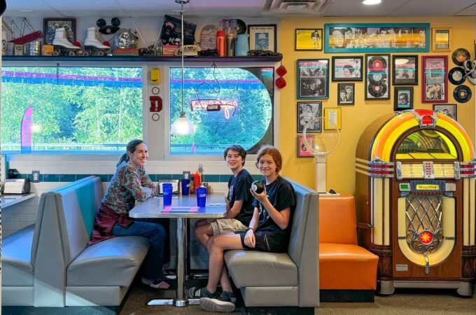 A family enjoys a meal at a retro 1950s diner in St. Paul, Minnesota. The interior features a classic jukebox, a surfboard, and vintage memorabilia on the shelves.