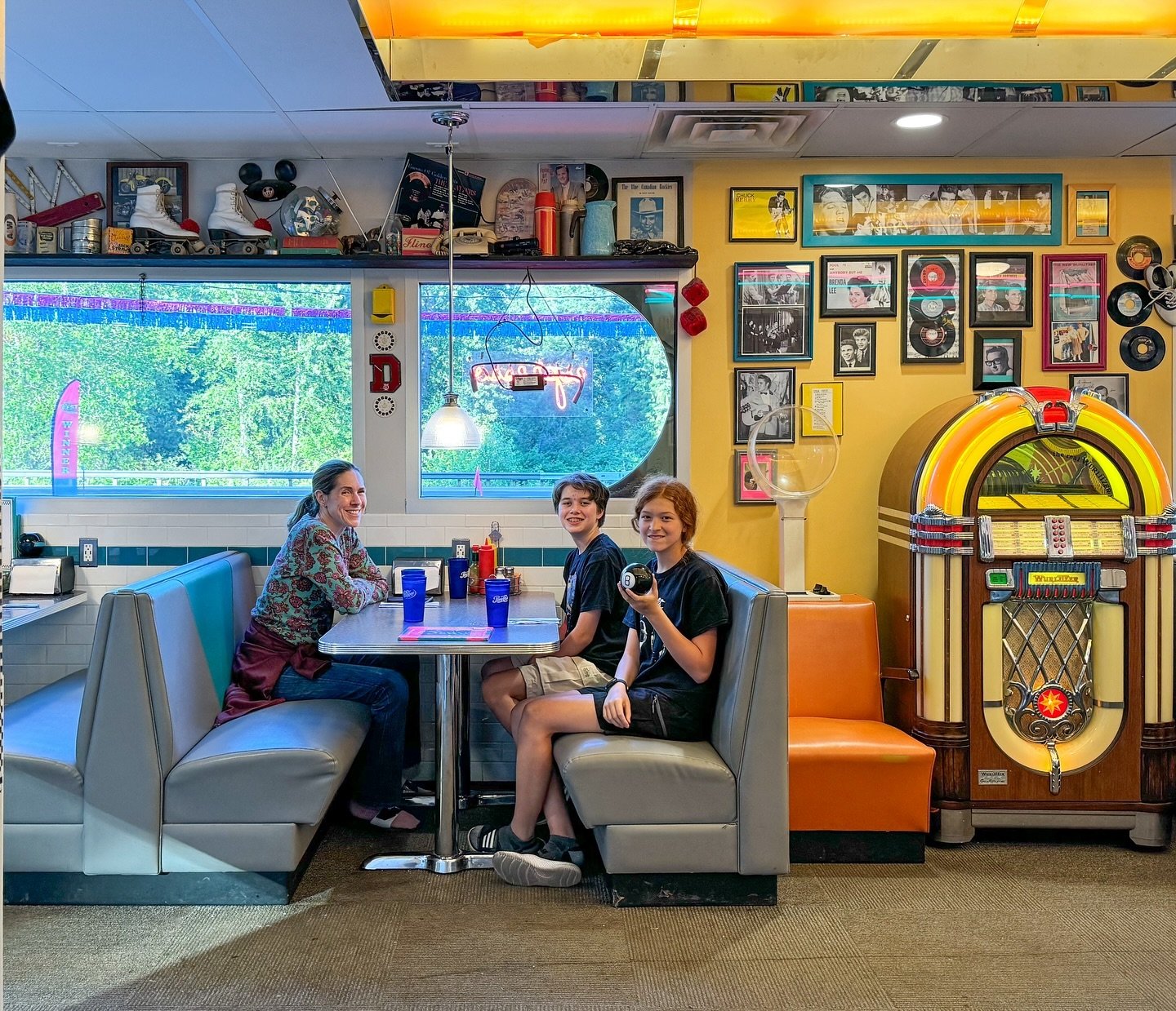 A family enjoys a meal at a retro 1950s diner in St. Paul, Minnesota. The interior features a classic jukebox, a surfboard, and vintage memorabilia on the shelves.