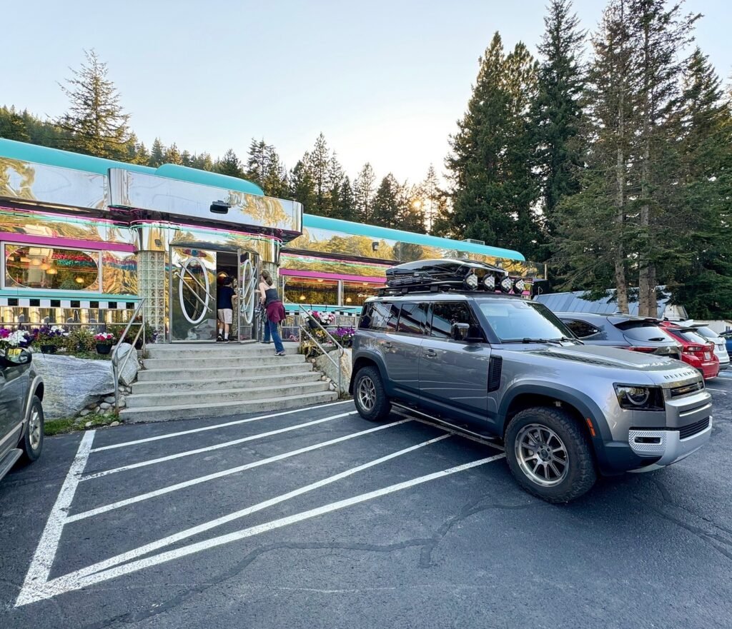 A silver Ford Bronco with a rooftop tent is parked in front of a mirrored lodge.