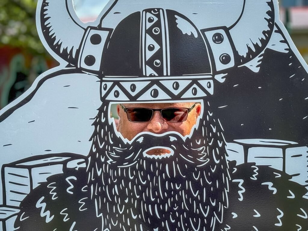A person peering through a hole in a large illustrated Viking cutout with a helmet and beard.