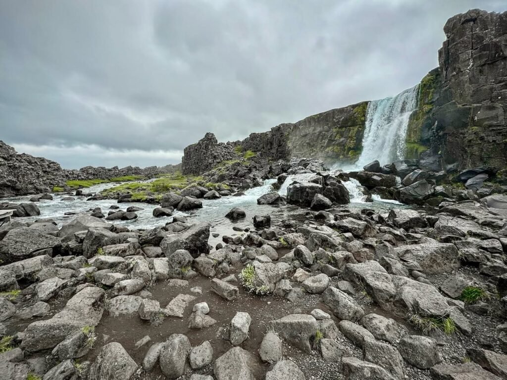 A scenic view of a waterfall and rocky terrain under a cloudy sky.