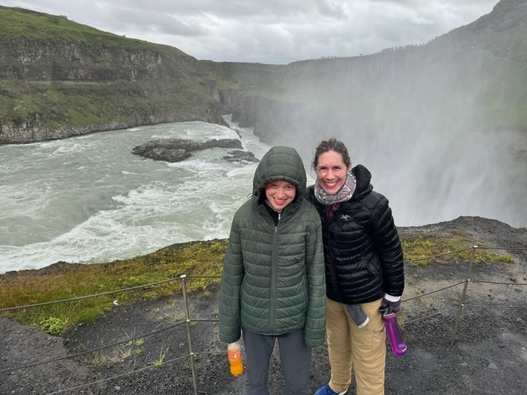 Two travelers enjoy the misty view of a powerful waterfall in Iceland.