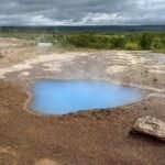 Gullfoss Waterfall A vibrant blue hot spring set against a rugged geothermal landscape under an overcast sky.