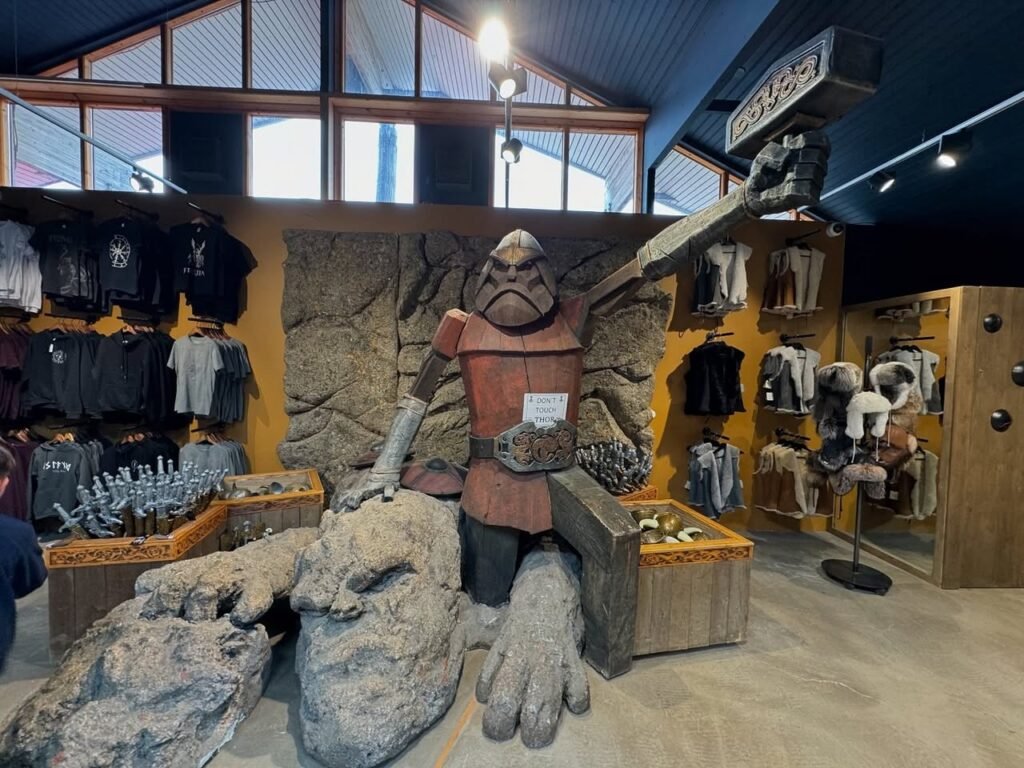 A stone statue of a rugged figure is displayed in a store with high ceilings and windows. The scene includes rock formations and gift cartons, set against a backdrop of hanging merchandise.