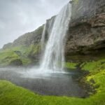 Skógafoss A tall waterfall cascades down a mossy cliff face into a dark pool surrounded by lush vegetation. Close-up views highlight the rugged texture of the surrounding rocks and vibrant green moss.