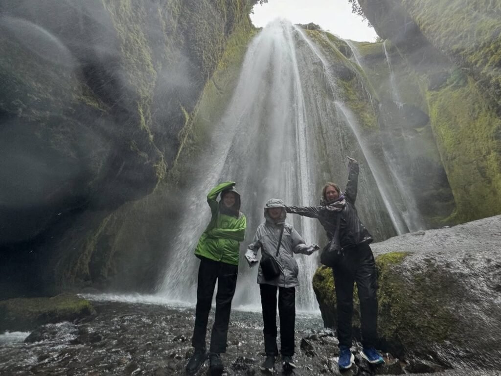Travelling through a misty waterfall cave in Iceland. A group of hikers braving the spray inside a mossy grotto.