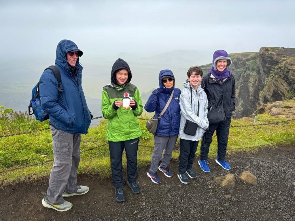 A group is posing in front of dramatic cliffs on a cloudy day. The visitors are dressed in colorful jackets, showcasing a scenic coastal area.