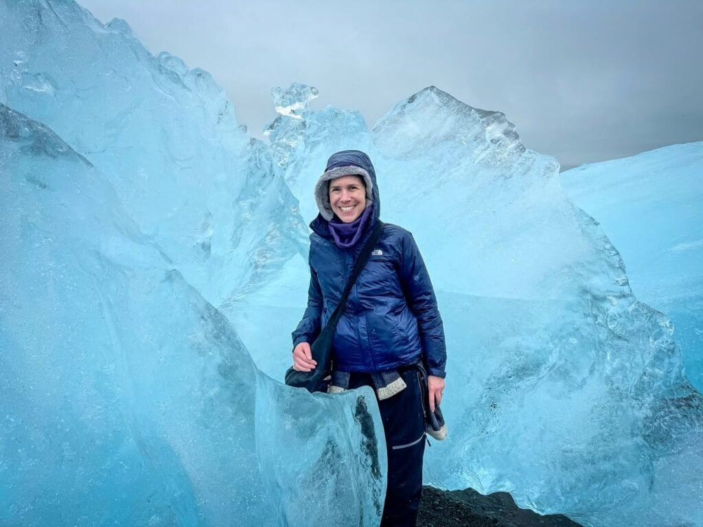 A traveler in winter gear poses amidst stunning turquoise glacier ice.