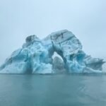 Vík í Mýrdal A large, sculpted blue iceberg featuring a natural arch floating in a misty arctic sea. A stunning polar scene captured during a remote travel expedition.