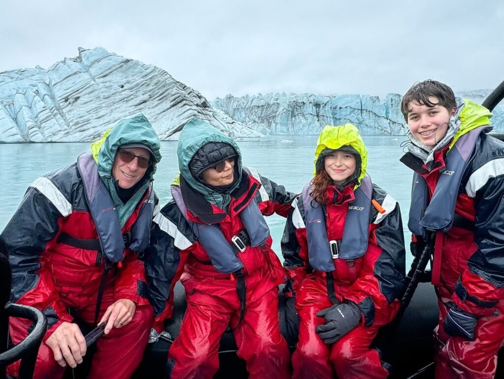 Four people in red waterproof gear on a boat paddling near a glacier