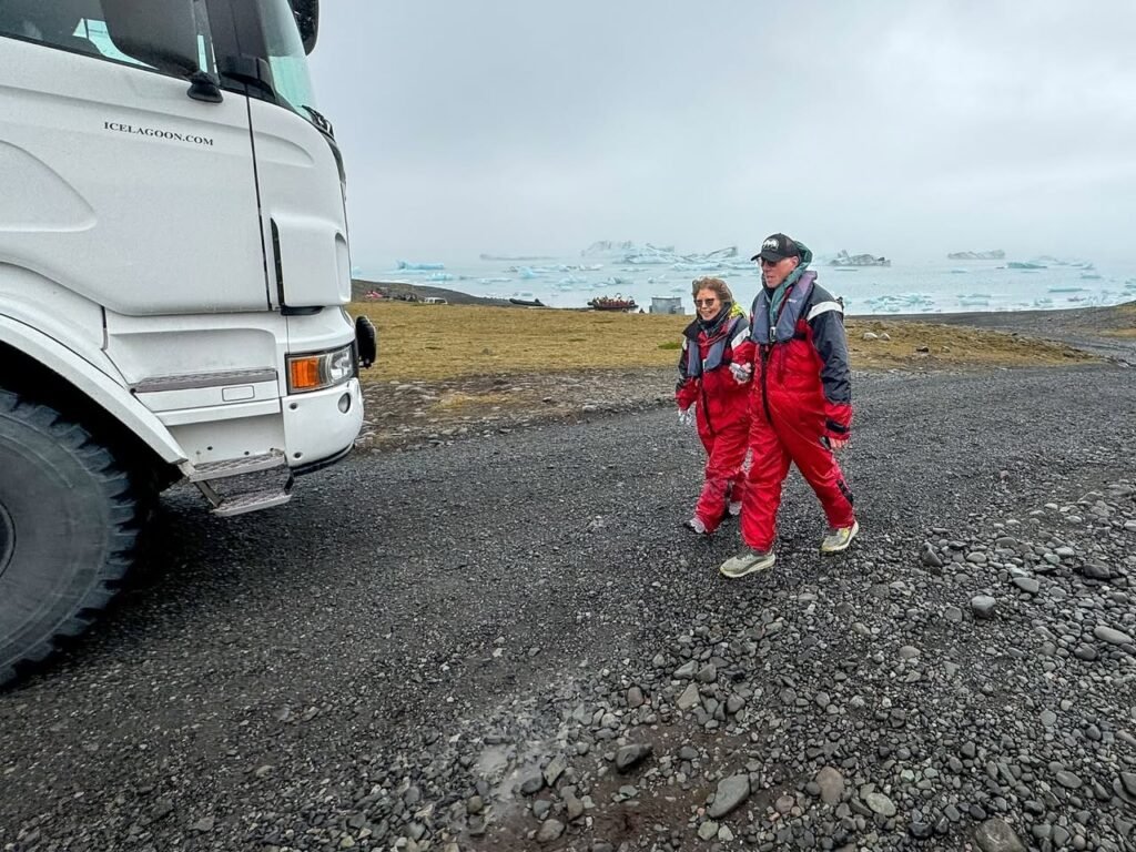 Two travelers in red parkas stand on a gravel road near an Arctic ship.