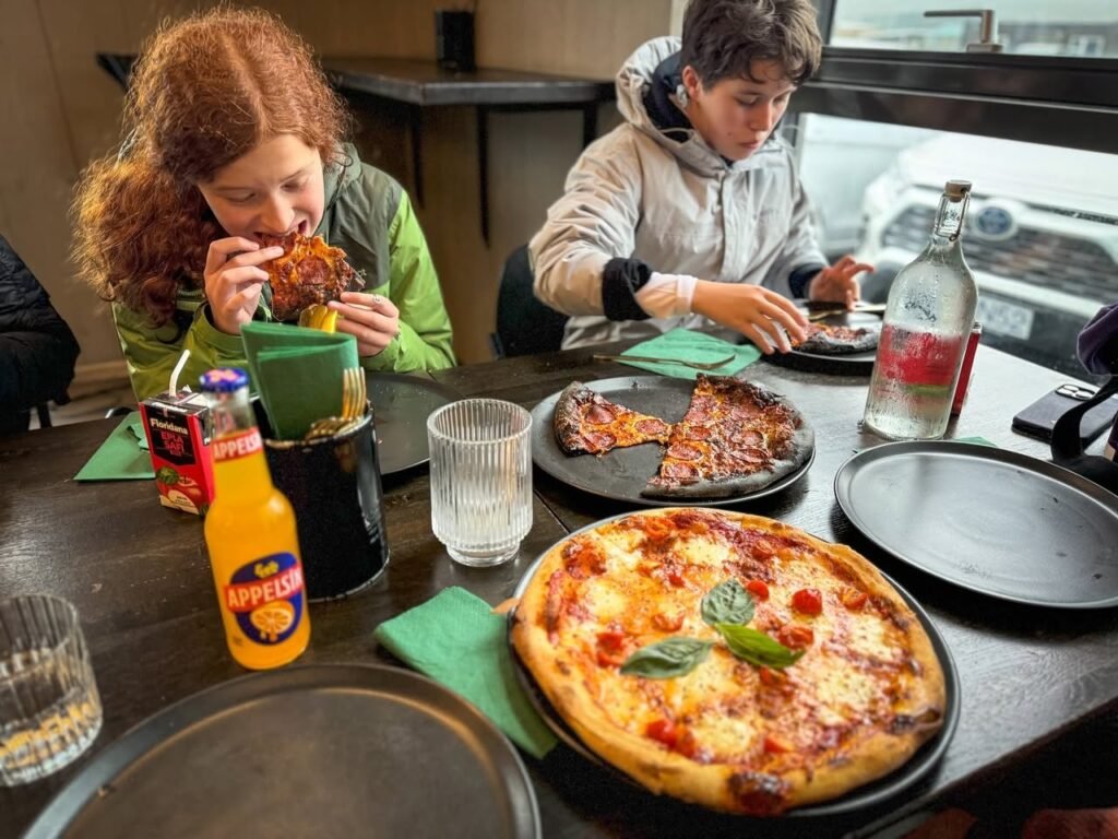 A table at a pizzeria with a pepperoni pizza and drinks, while two people enjoy a meal together.