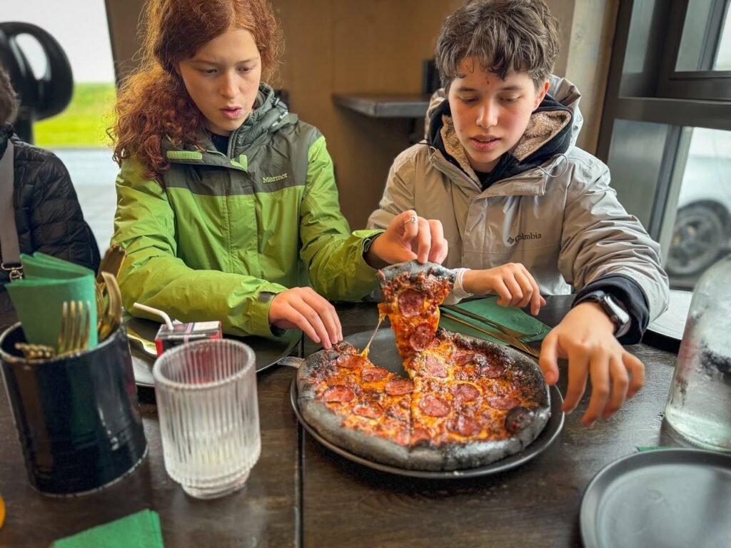 Two people in parkas enjoy a cheesy pizza at a cozy restaurant.