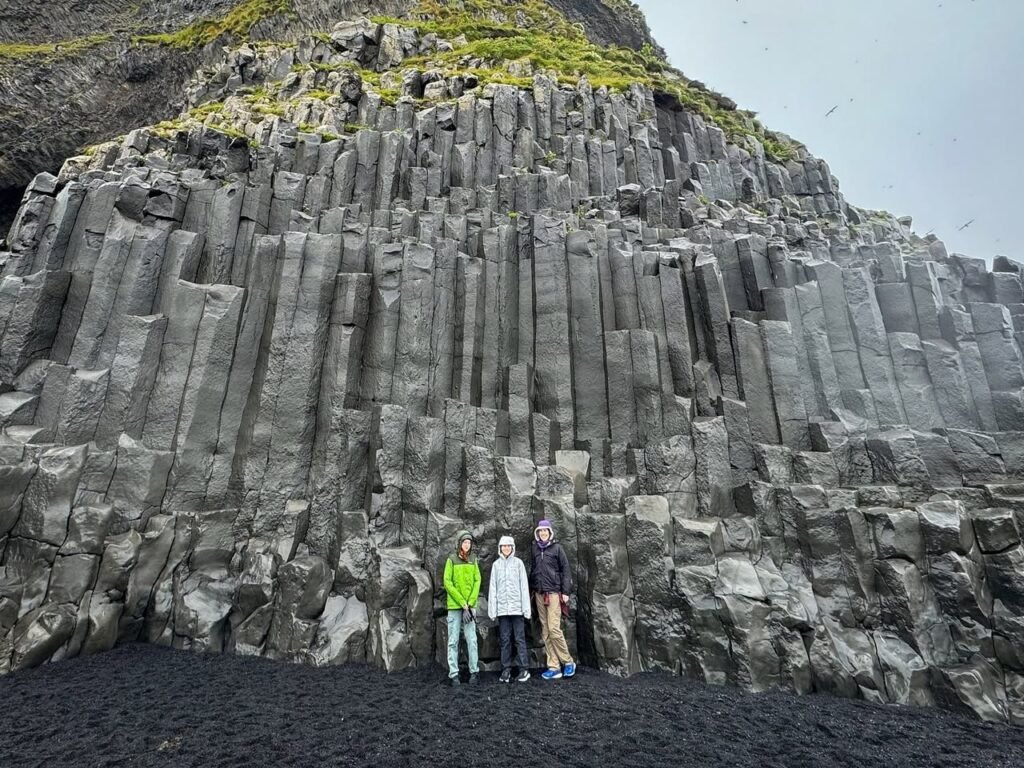 A group of hikers standing before towering hexagonal basalt columns. Close-up view of the vertical rock formations.