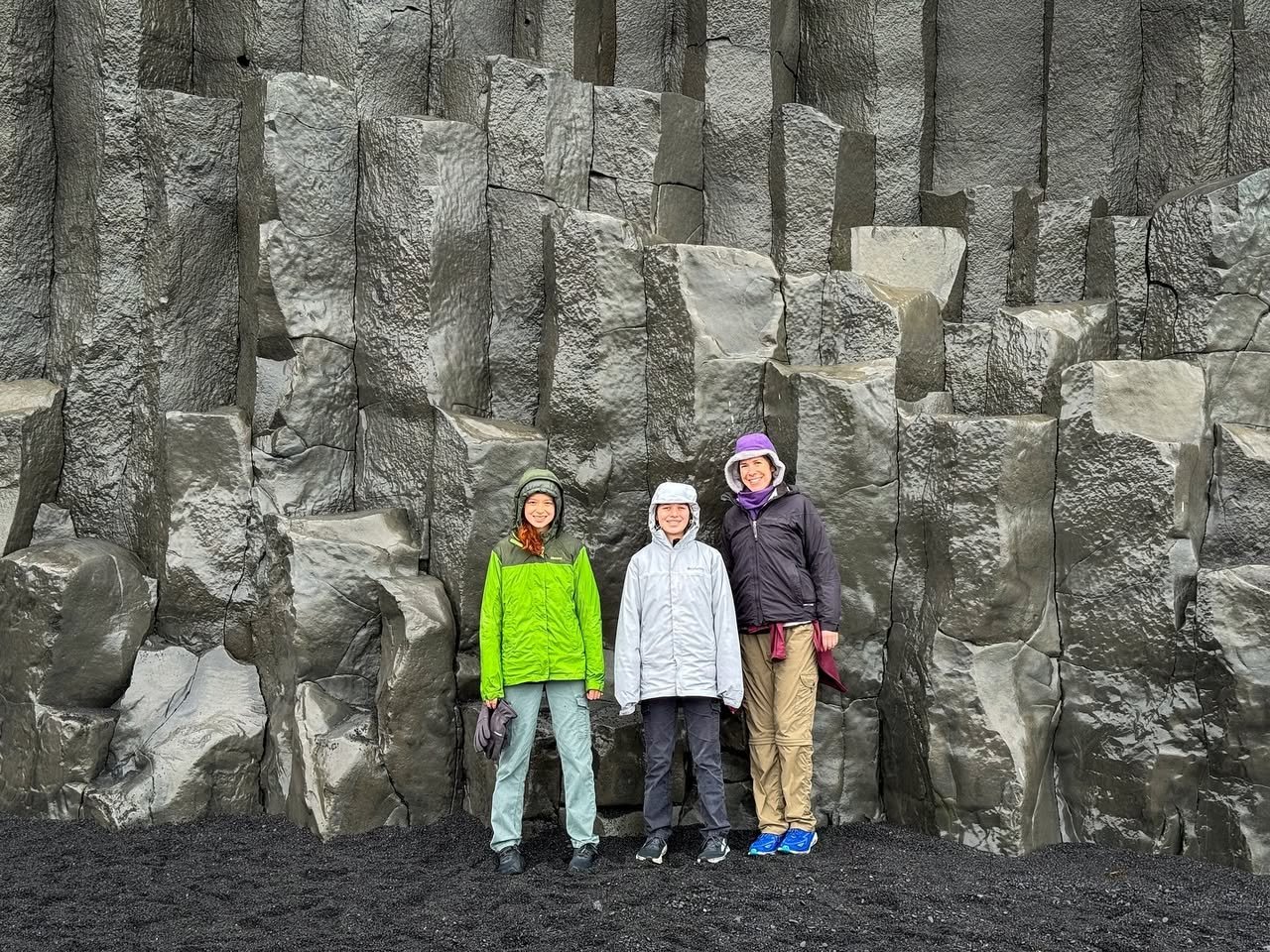 Vík í Mýrdal Three visitors stand in front of the basalt columns at the Giant's Causeway in Northern Ireland. The scene captures a family moment at a famous geological landmark.