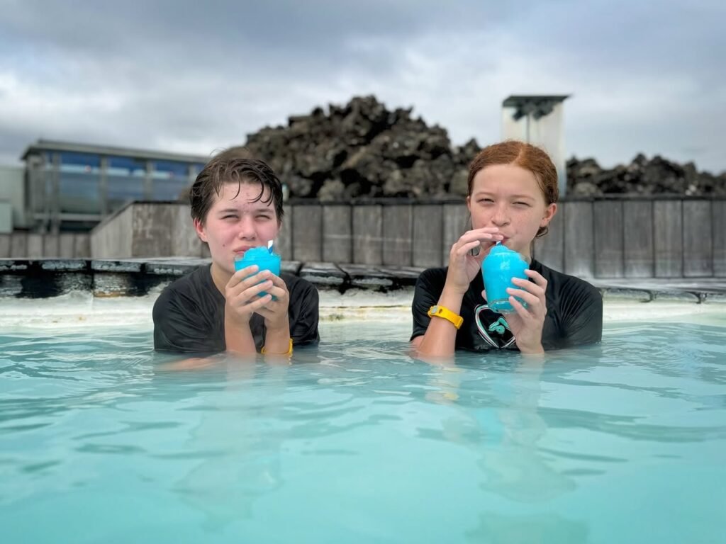 Two people relaxing in a milky blue hot springs pool while drinking from blue cups.