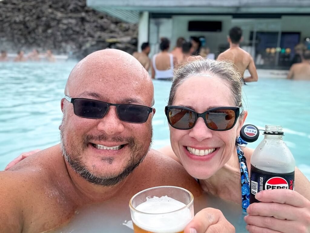 A couple enjoying a hot spring with drinks and a view of the pool.