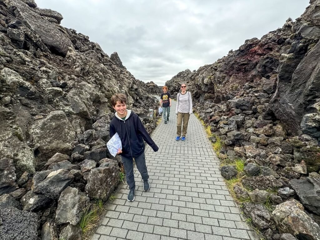 A paved walking path cutting through a rugged rock formation under a cloudy sky.