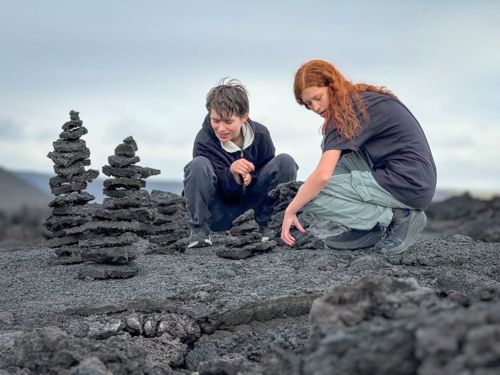 Two people crouching on a dark, rocky terrain, stacking stones into intricate spiral formations known as lethis.