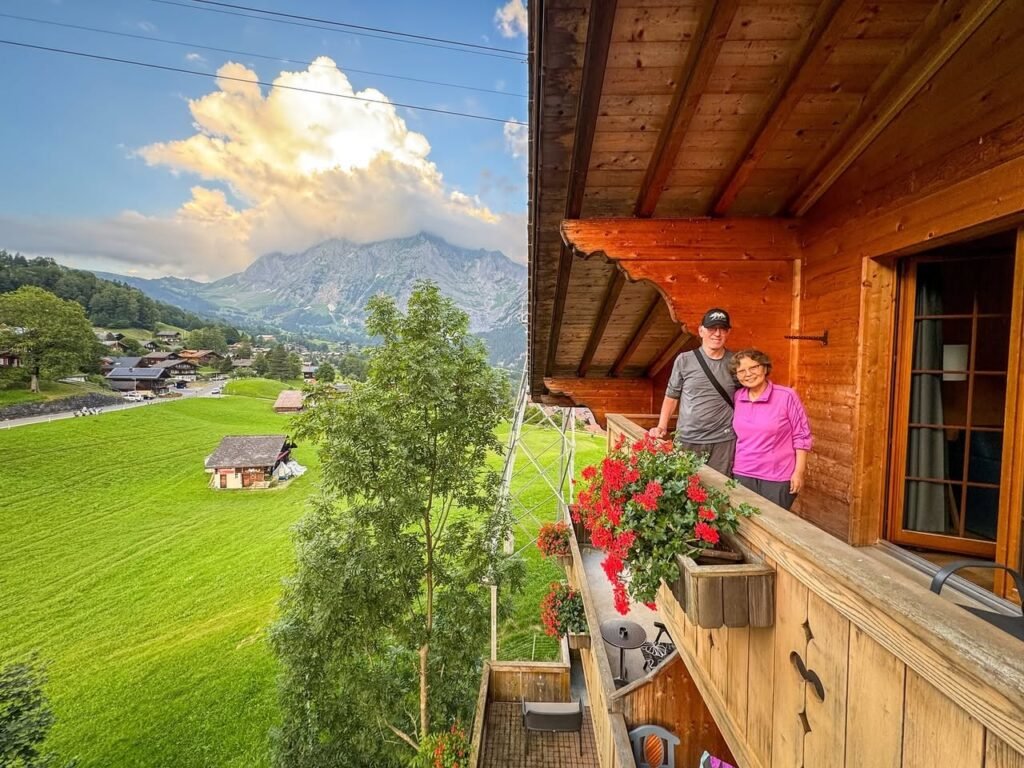 A wooden cabin balcony overlooking lush green fields and mountains.