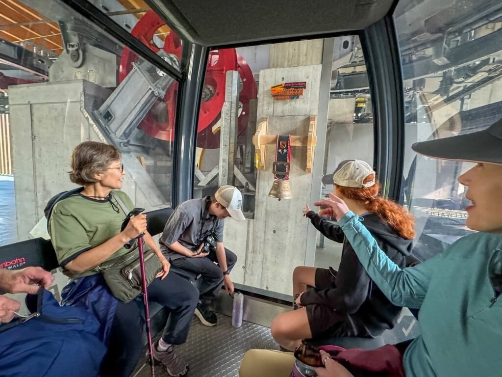 Travelers share a moment inside a glass-enclosed mountain ropeway looking out at the steep terrain. This scene captures a high-altitude journey with scenic views.