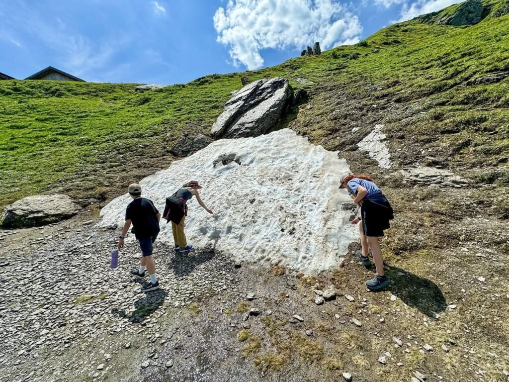 Hikers explore a large rock formation on a sunny day in a grassy area, with a large boulder in the background.