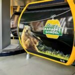 Alpine Sensation A yellow and black gondola car featuring a graphic of the Ricola Karaoke Gondol and a singing marmot.