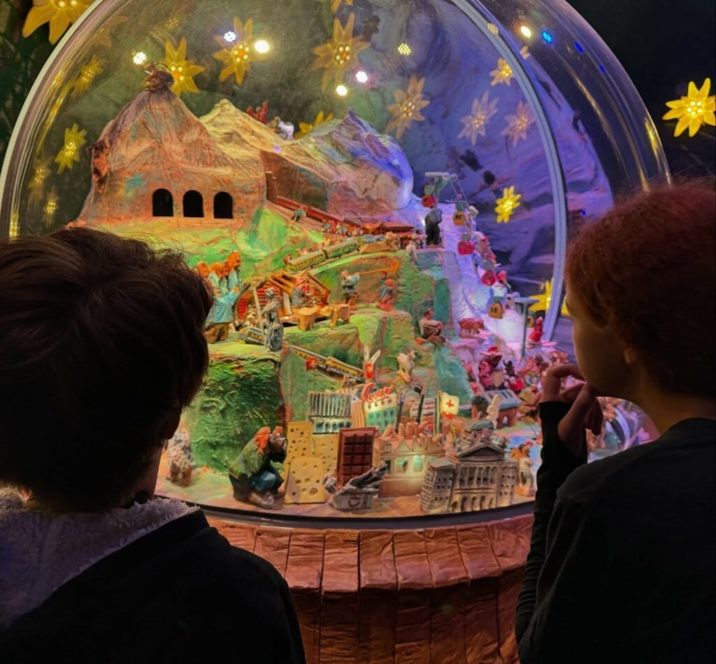 People viewing a colorful miniature Nutcracker House diorama inside a glass dome decorated with golden stars.