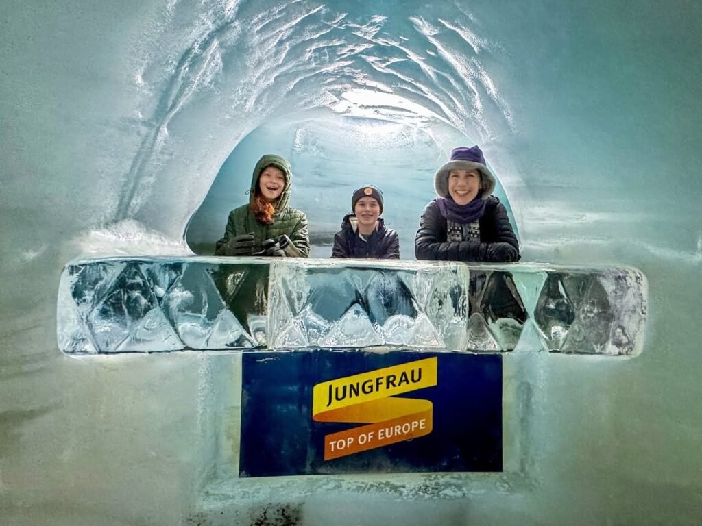 People smiling from an observation window inside the icy Jungfraujoch tunnel, viewing the Swiss Alps.