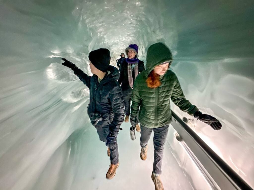 Visitors in winter clothing explore a stunning tunnel carved into a glacier's blue ice.
