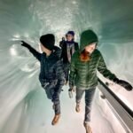 Alpine Sensation Visitors in winter clothing explore a stunning tunnel carved into a glacier's blue ice.