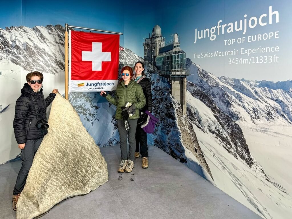 Travelers pose with a Swiss national flag in front of a mural at Jungfraujoch, the top of Europe.