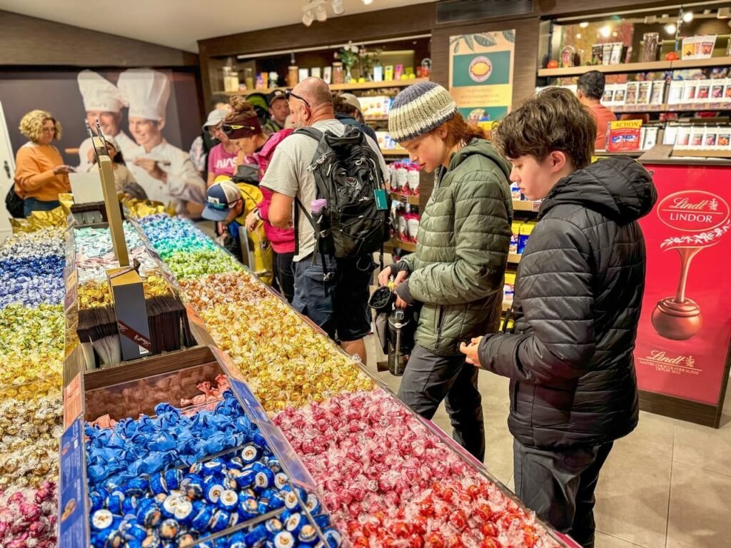 Customers browse a colorful display of wrapped chocolates at a busy European confectionery shop.