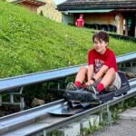 Schynige Platte A person enjoying a luge ride on a metal track winding through a green hillside, with a luge station visible in the background.