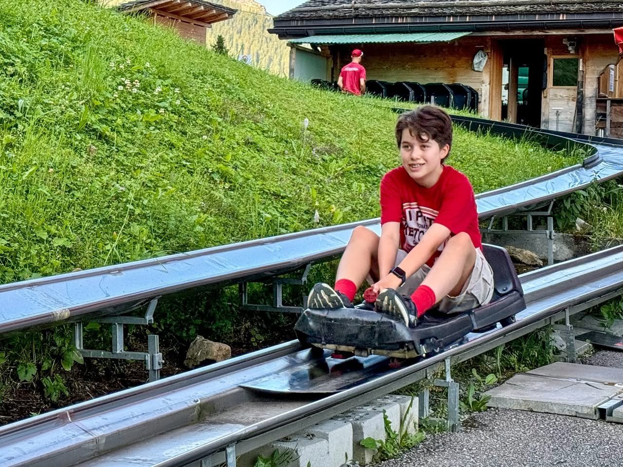 Pfingstegg A person enjoying a luge ride on a metal track winding through a green hillside, with a luge station visible in the background.