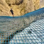 Pfingstegg A person walks on a blue metal grid bridge suspended against a rocky cliff face.