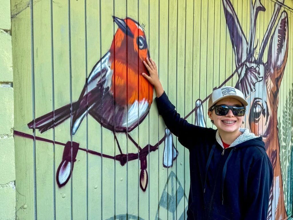 A happy person enjoys a colorful outdoor mural featuring a bird and rabbit. The playful street art adds a vibrant touch to the neighborhood.