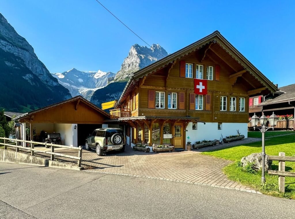 A traditional wooden chalet with a Swiss cross set against the backdrop of the Matterhorn and glaciers in Zermatt, Switzerland. The second photo highlights the iconic mountain peak, while closer views show the lodge's architecture and parking area.