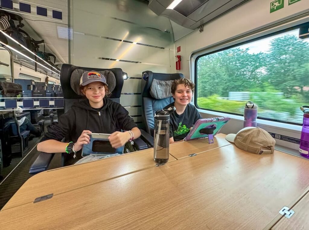 Passengers enjoying a train trip through a scenic green landscape, using tablets and enjoying the view.