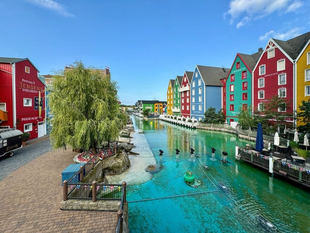 A scenic canal lined with vibrant, colorful Scandinavian-style buildings. The water features fountains and a waterfront cafe at this picturesque tourist spot.