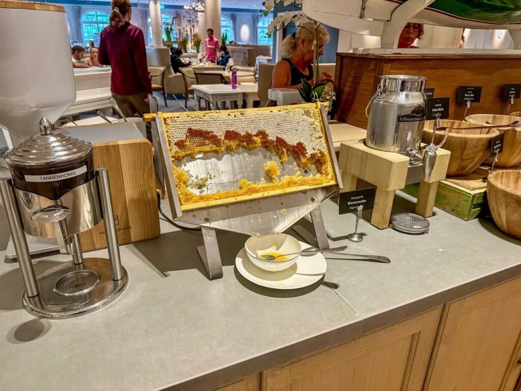 Breakfast station in an airport terminal with pastries and beverages. A person is visible in the background near tables.