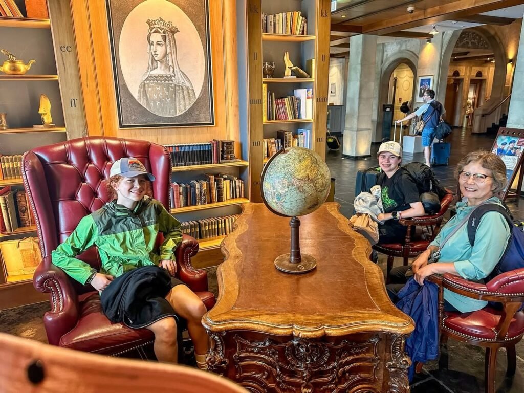 People relaxing in red leather chairs around a table with a globe in a historic library.