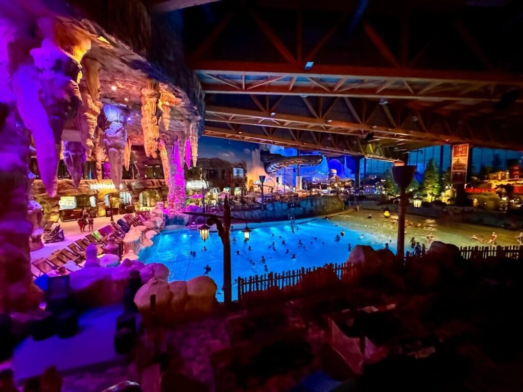 An indoor pool glowing blue and purple under a cave-like ceiling. Stone archways and lighting create a magical nighttime atmosphere.
