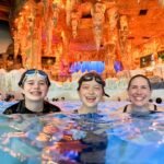 Europa-Park Visitors enjoying warm waters in a hot spring surrounded by an illuminated ice-like cave interior, featuring textured walls and colorful lighting.