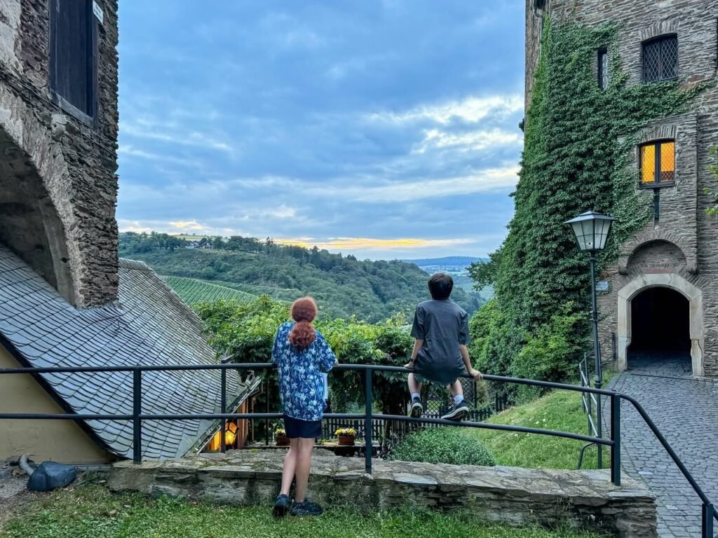 A stone castle courtyard leading to a panoramic valley view at sunset.