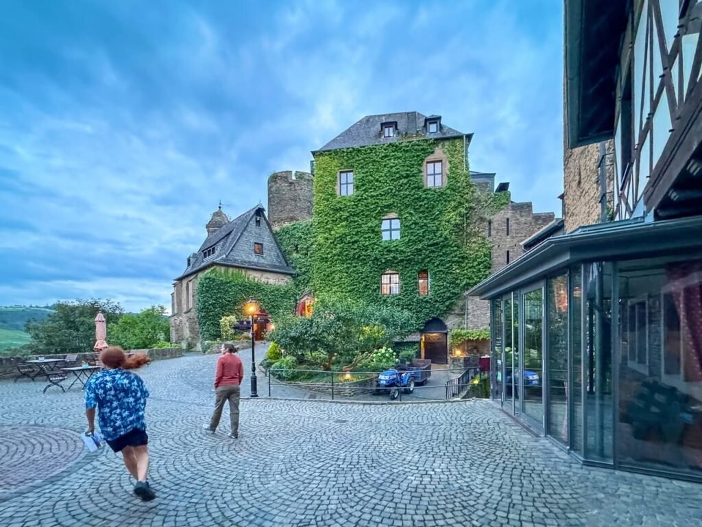 A picture-collage view of a cobblestone plaza with a moss-covered castle tower and half-timbered buildings.