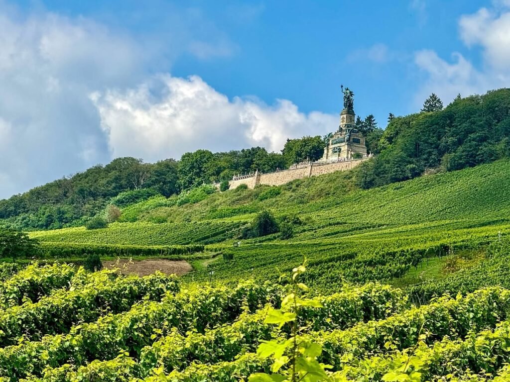 A hilltop monument stands above rolling vineyards under a bright blue sky with scattered clouds.