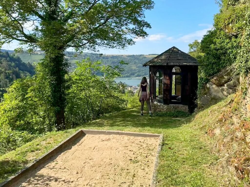 A wooden cabin nestled among lush trees with expansive views of forested hills and distant mountains under a clear blue sky.