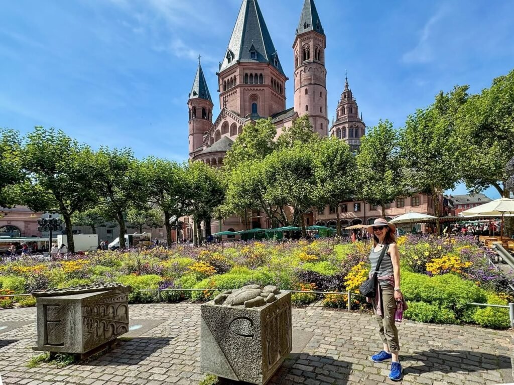 A visitor enjoys the blooming gardens in front of Prague's iconic St. Vitus Cathedral, with detailed stone planters in the foreground and a clear blue sky overhead.